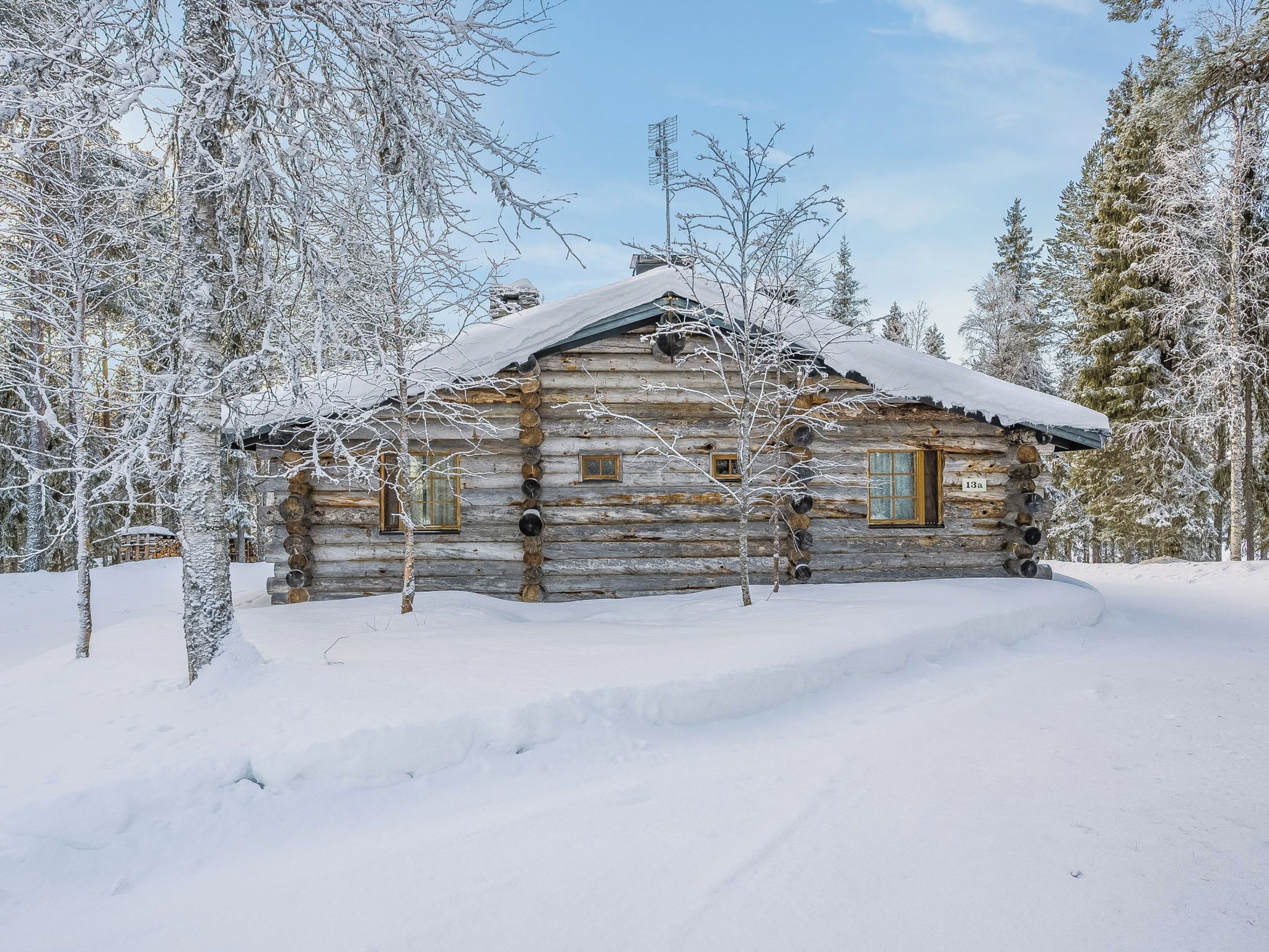 Una cabaña de troncos con techo nevado, rodeada de árboles cargados de nieve.
