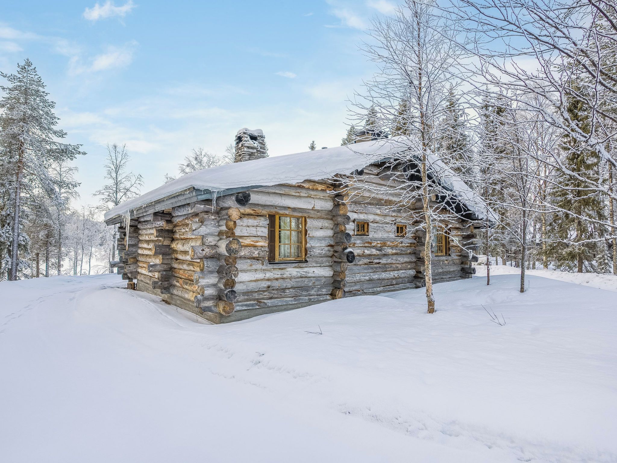 Una cabaña de troncos con techo nevado, rodeada de árboles cubiertos de nieve.