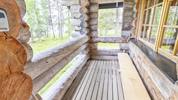 Het interieur van een blokhut met een houten bank, een raam met uitzicht op het bos en een stenen muur.