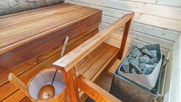 A sauna with a wooden bench, a bucket with a ladle, and a container of stones.