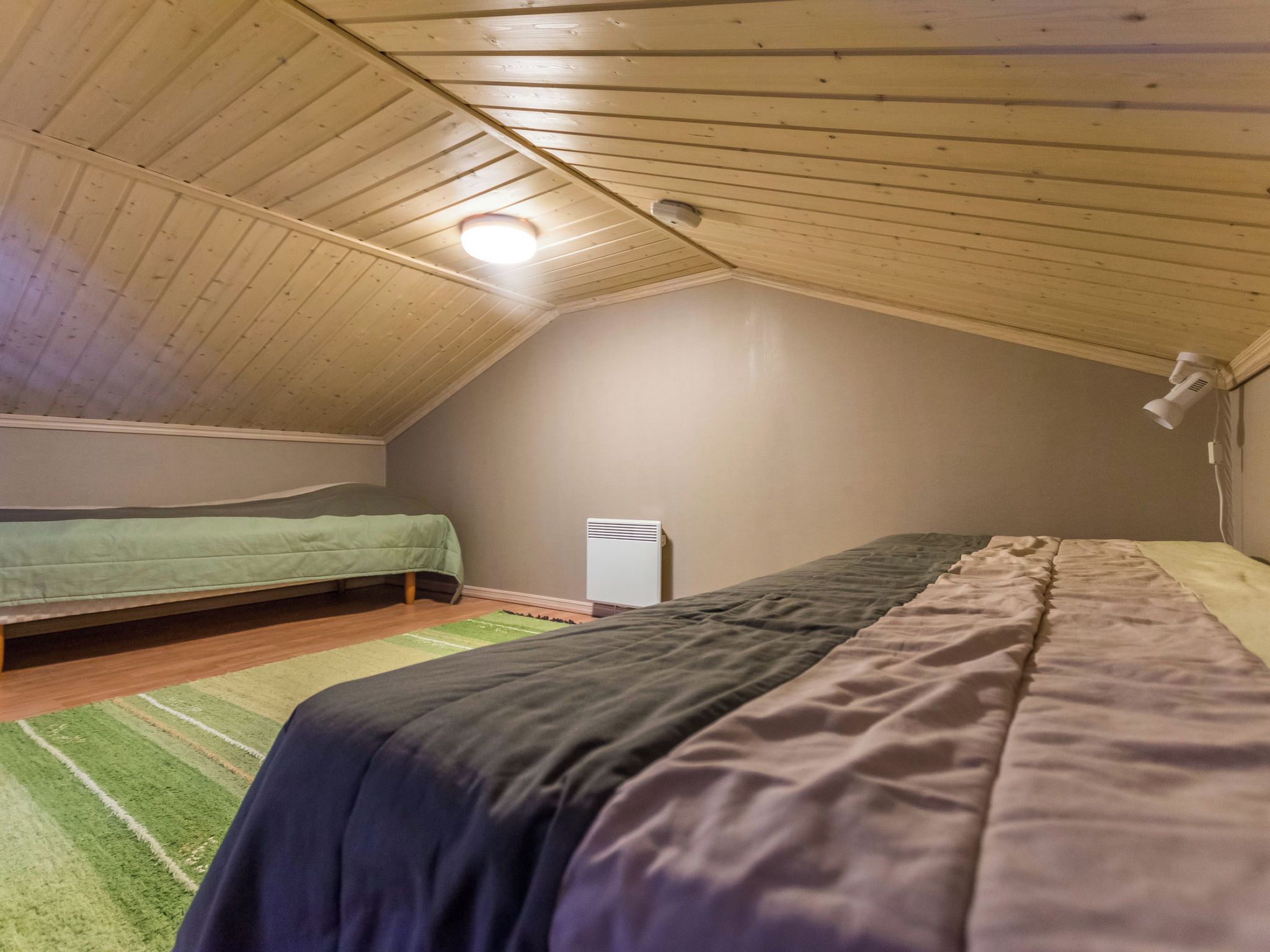 Ein Zimmer mit schrägem Dach, zwei Betten, einem Heizgerät und einer Wandleuchte.