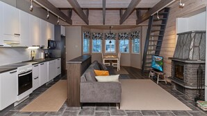 A modern kitchen with white cabinets and a built-in oven, a gray sofa with a throw pillow, a fireplace with a stone surround, and a television on a stand.