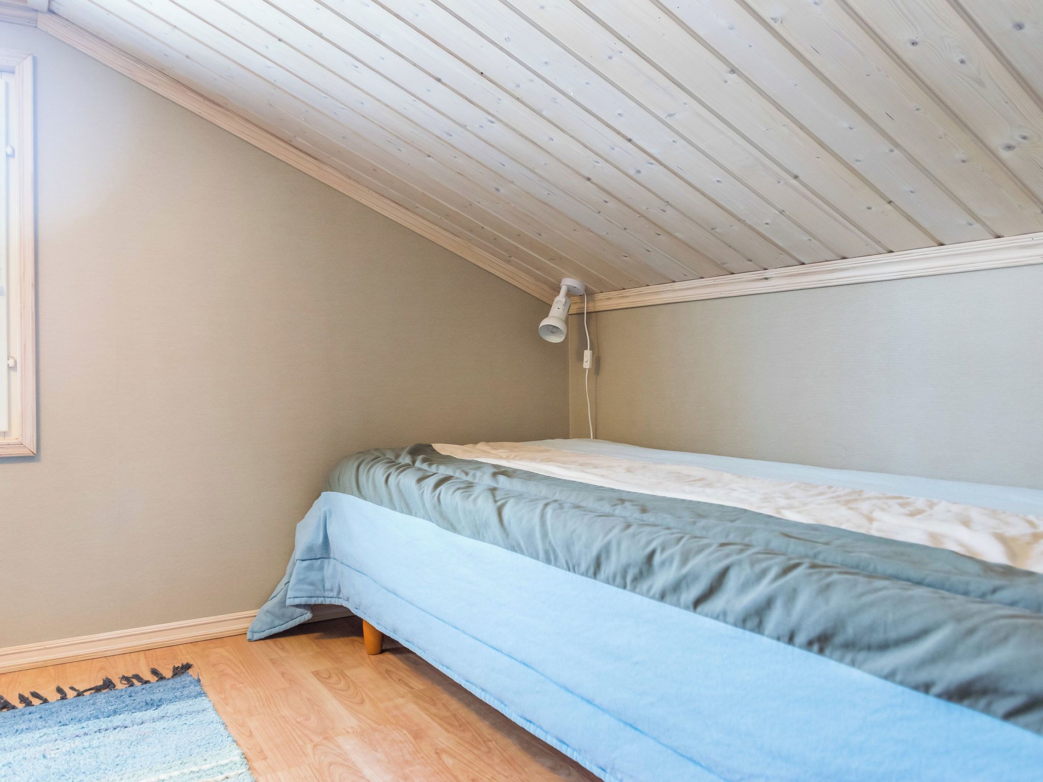 Une petite chambre avec un lit simple, un plafond en pente et une fenêtre sur le côté gauche.