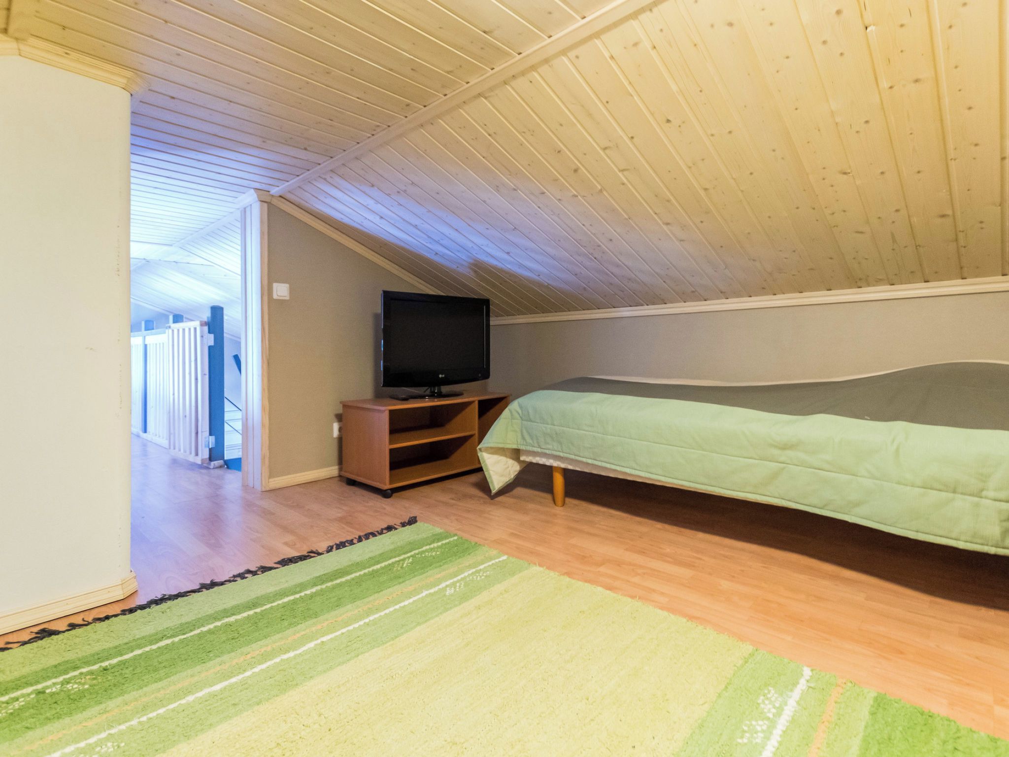 Ein Zimmer mit einem Bett, einem Fernseher auf einem Schrank und einem Gang zu einem weiteren Raum.