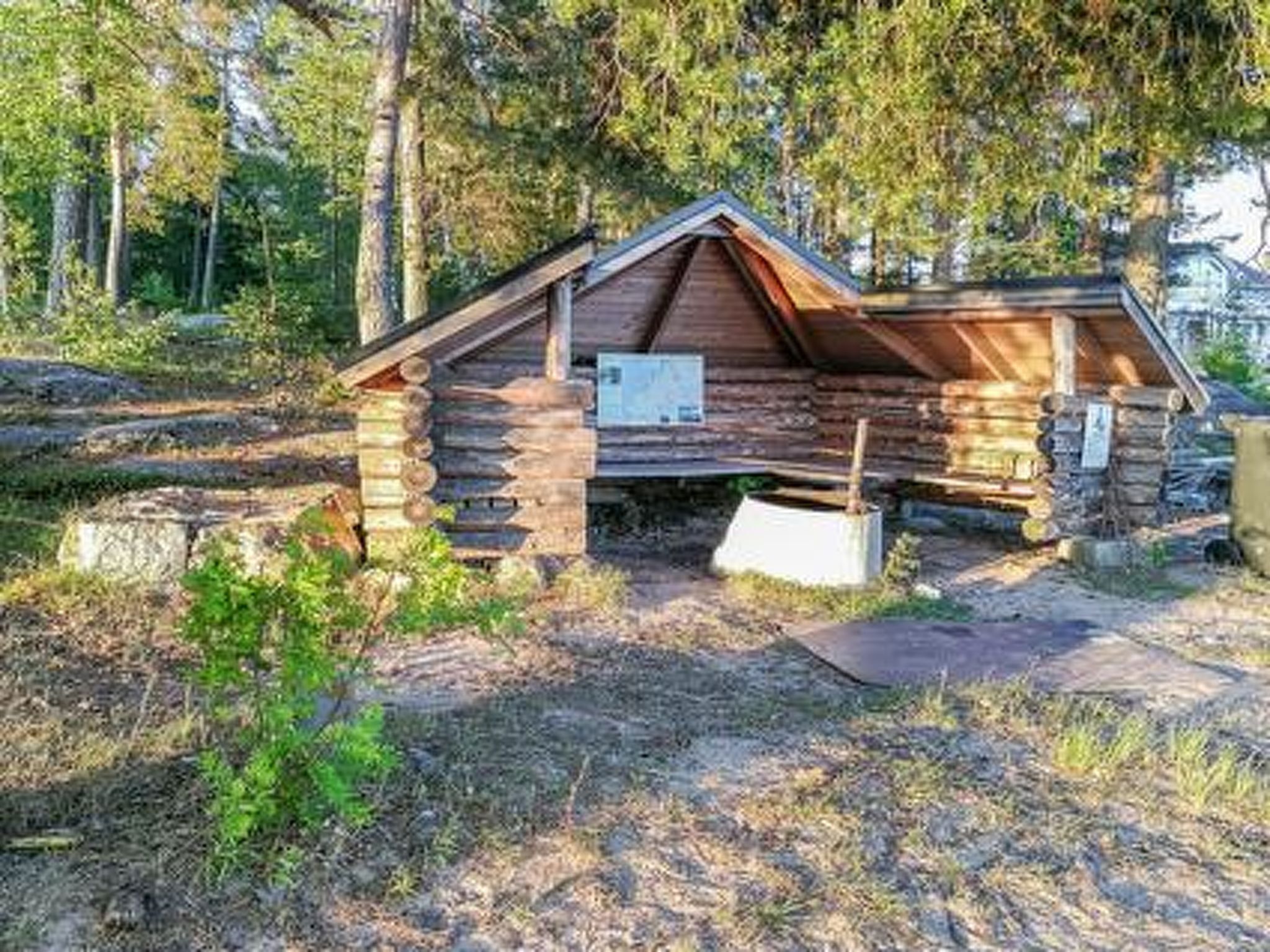 Tunnelmallinen hirsihökkelö, jossa on jyrkkäkattoinen katto ja jonka ympärillä on puita.