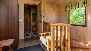 L’intérieur d’un chalet en bois, avec un banc en bois, une porte donnant sur une salle de bain et une fenêtre offrant une vue sur la verdure.