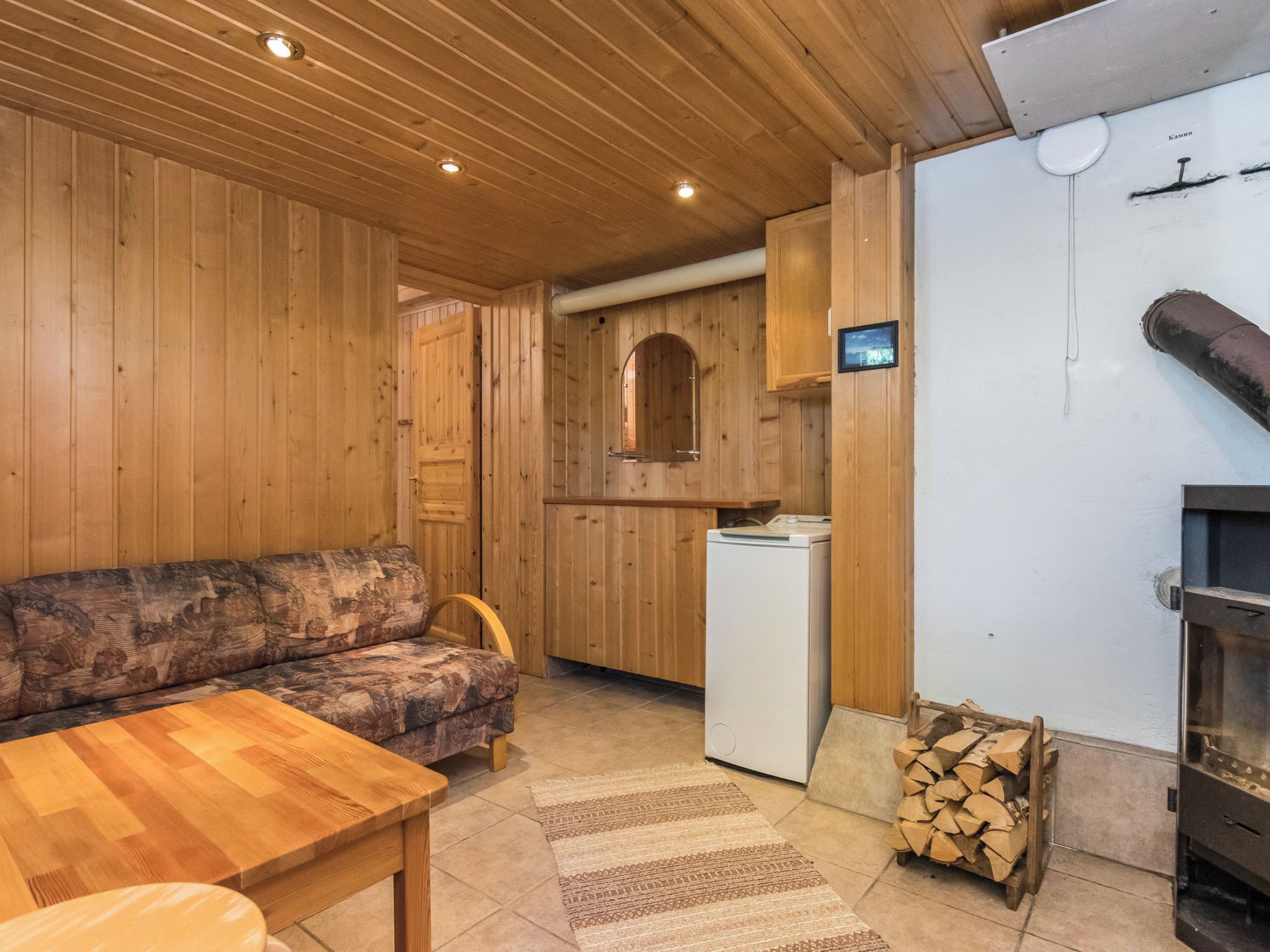 A wooden interior with a sofa, a table, a kitchen area with a refrigerator, and a fireplace.