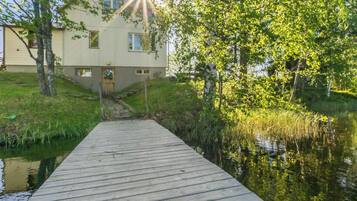 A wooden dock leading to a house with a grassy area and trees around.