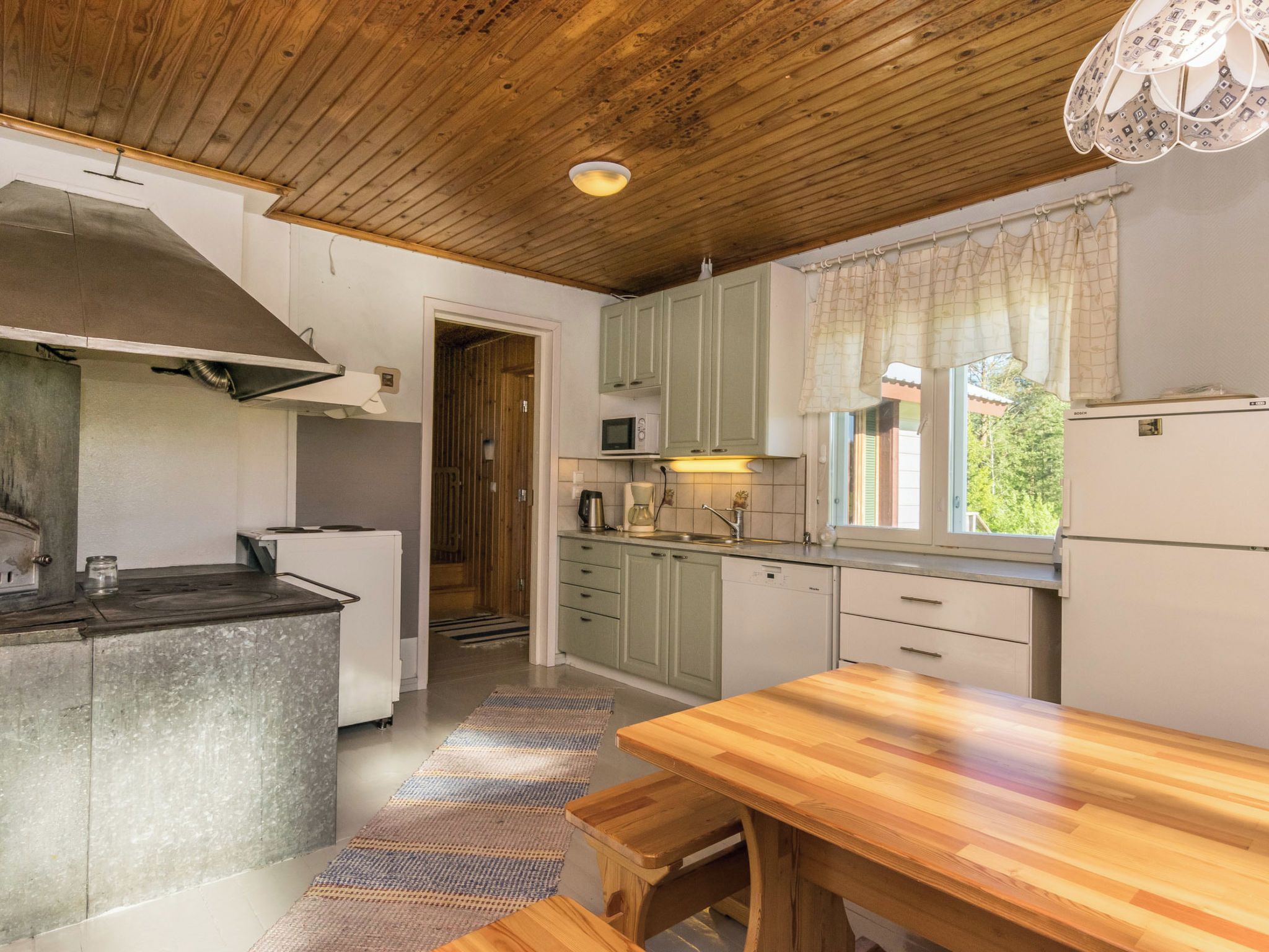 A compact kitchen with a wooden ceiling, a built-in stove, a microwave, and a refrigerator.