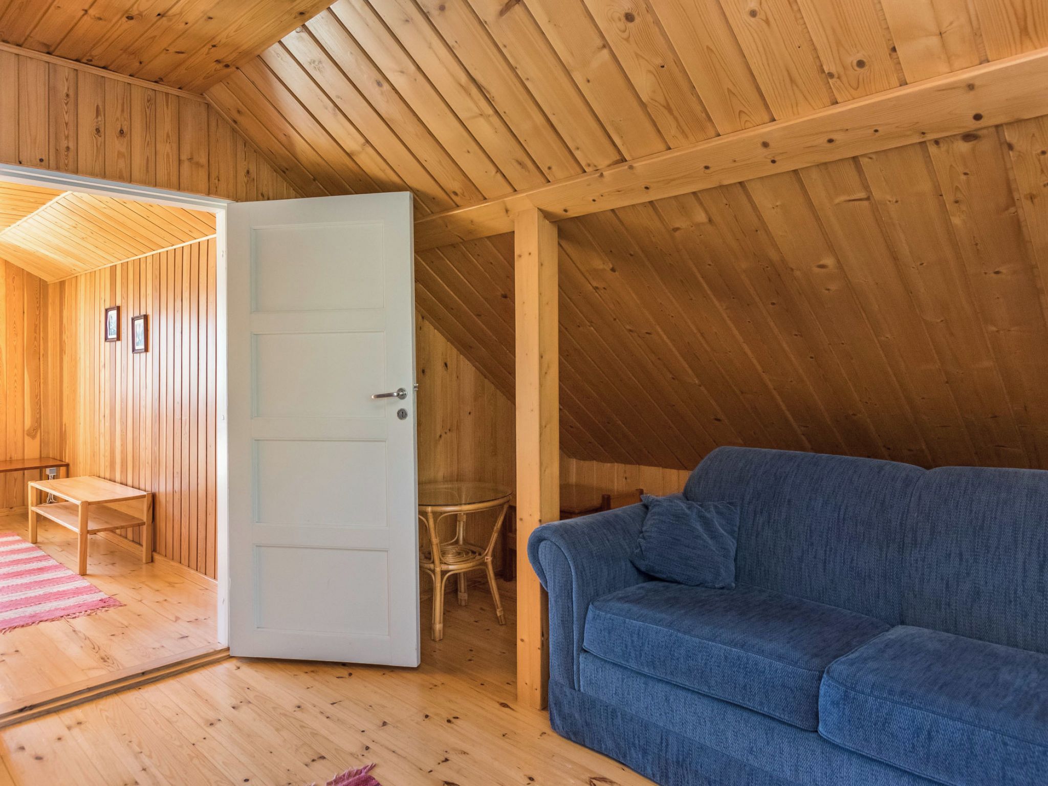 Un intérieur en bois avec un canapé bleu, une porte donnant sur une autre pièce et une petite table.