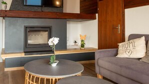A modern living room with a fireplace, a round table with a potted plant, a sofa with a cushion, and a wooden door. - Zurschmitten 17 1. OG Süd by Interhome (Riederalp)