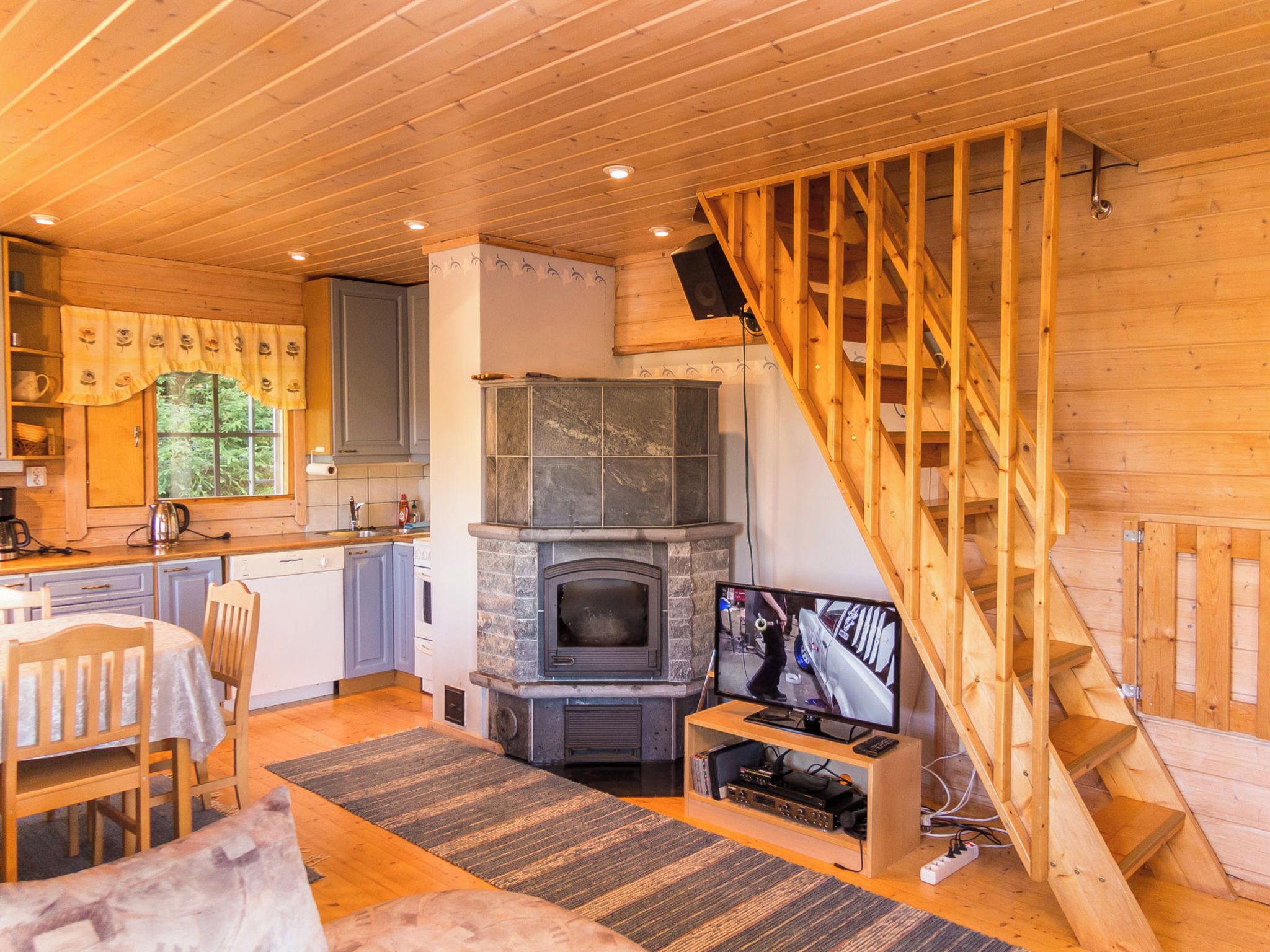 Een gezellig blokhutinterieur met een keuken, eethoek, open haard en een houten trap.