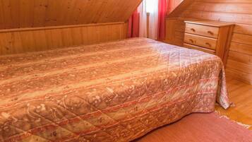 A bedroom with a wooden ceiling, a bed with a patterned bedspread, a wooden dresser, and a red curtain.