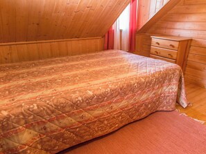 A bedroom with a wooden ceiling, a bed with a patterned bedspread, a wooden dresser, and a red curtain. - Iltarusko by Interhome (Nilsiä)