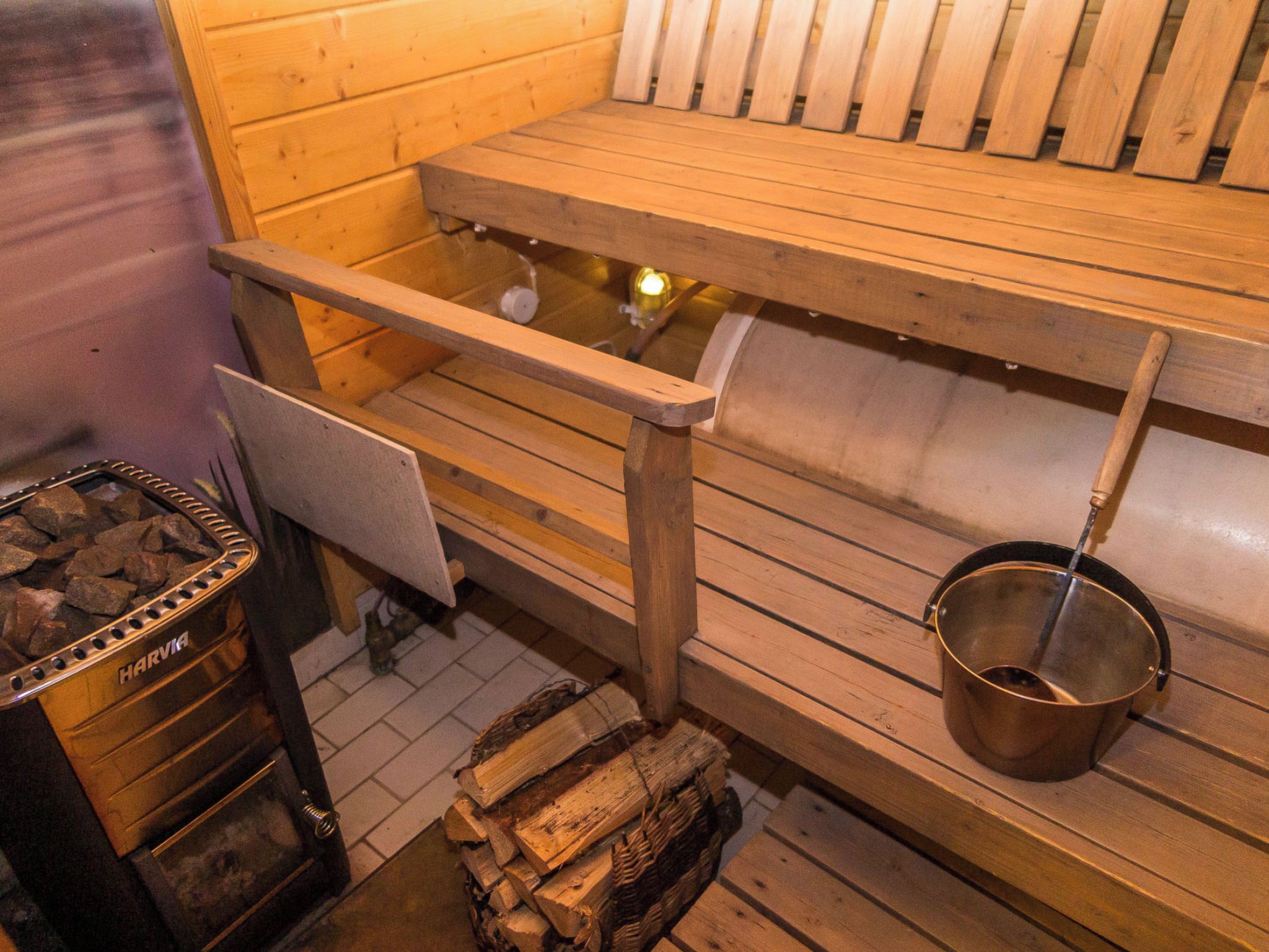 Una sauna con bancos de madera, un recipiente metálico para agua y un horno de leña.