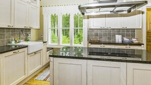 Une cuisine avec des armoires blanches, un plan de travail noir, une hotte de cuisine en acier inoxydable et une fenêtre donnant sur des arbres.