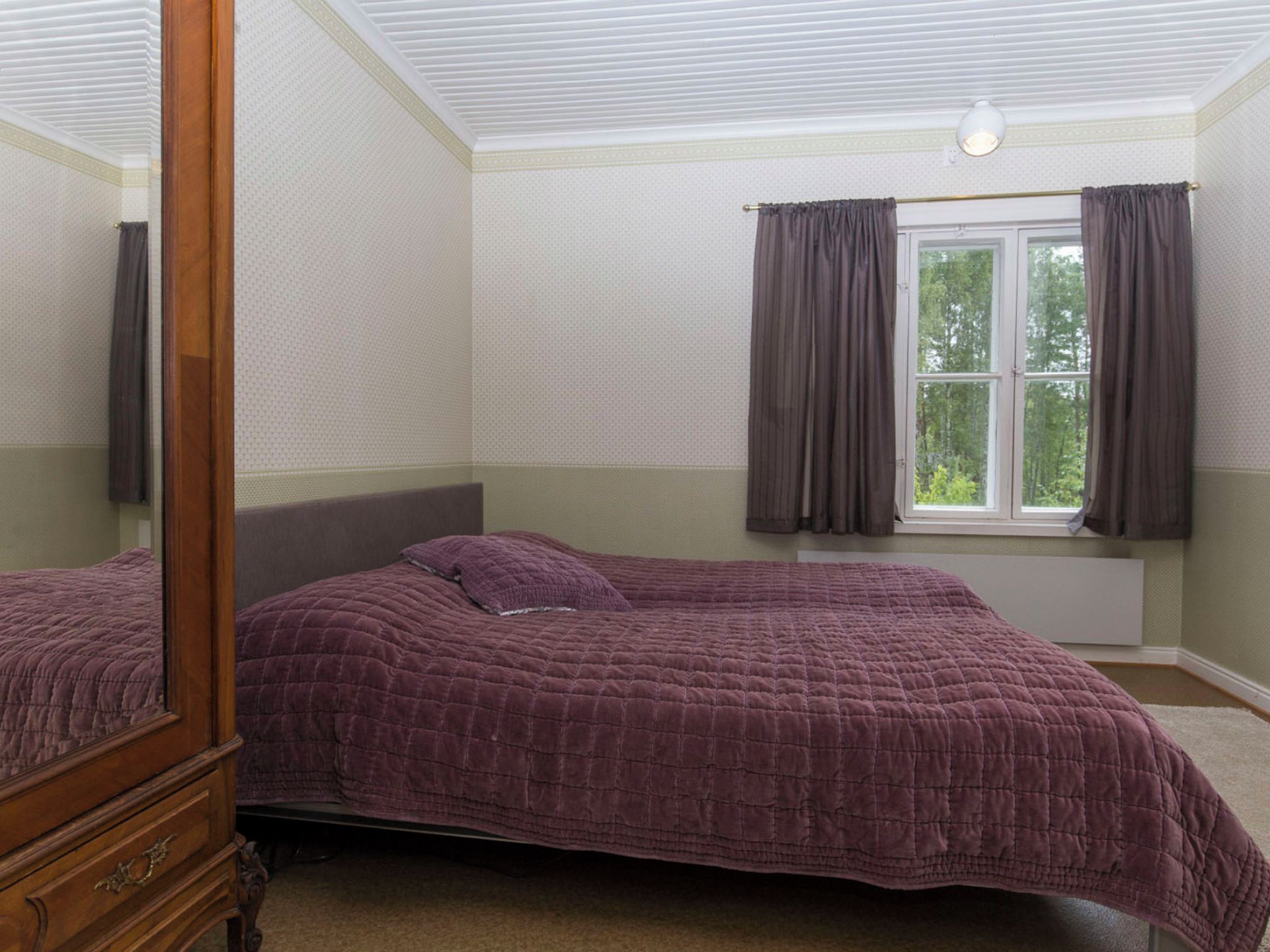A bedroom with two beds, a window with curtains, and a mirror.