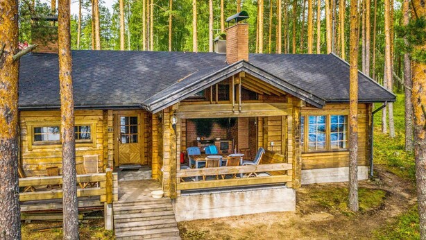 Une cabane en bois avec une véranda, une cheminée et un coin repas.