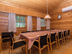 L’intérieur d’un chalet en bois, avec une table à manger, des chaises, un luminaire suspendu et une horloge au mur.