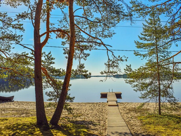 A wooden dock leading to a calm lake, surrounded by trees and a clear sky.