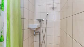 Eine kleine, geflieste Duschkabine mit einer Handbrause und einem am Wand montierten Wasserhahn.