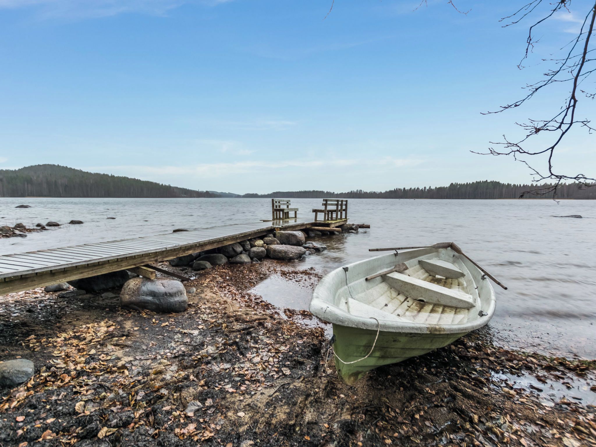 Une jetée en bois s’étendant dans un lac paisible, avec une barque à rames et des bancs à son extrémité.