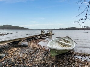 Une jetée en bois s’étendant dans un lac paisible, avec une barque à rames et des bancs à son extrémité.