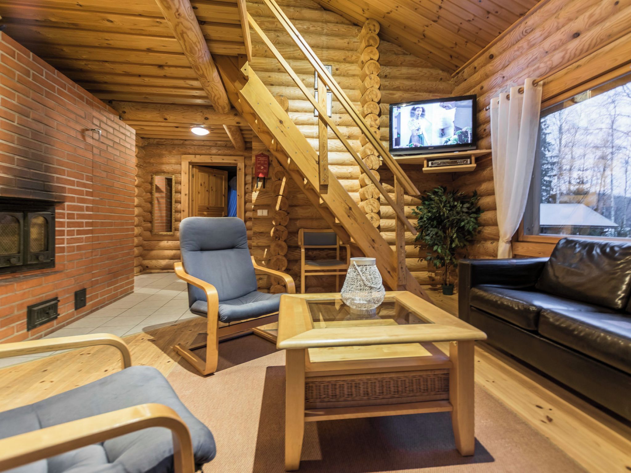A log cabin interior with a fireplace, a television, a staircase, and a sofa.