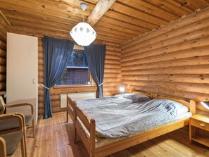 Une pièce de cabane en bois comprenant un lit, une chaise, un bureau et une fenêtre avec des rideaux.