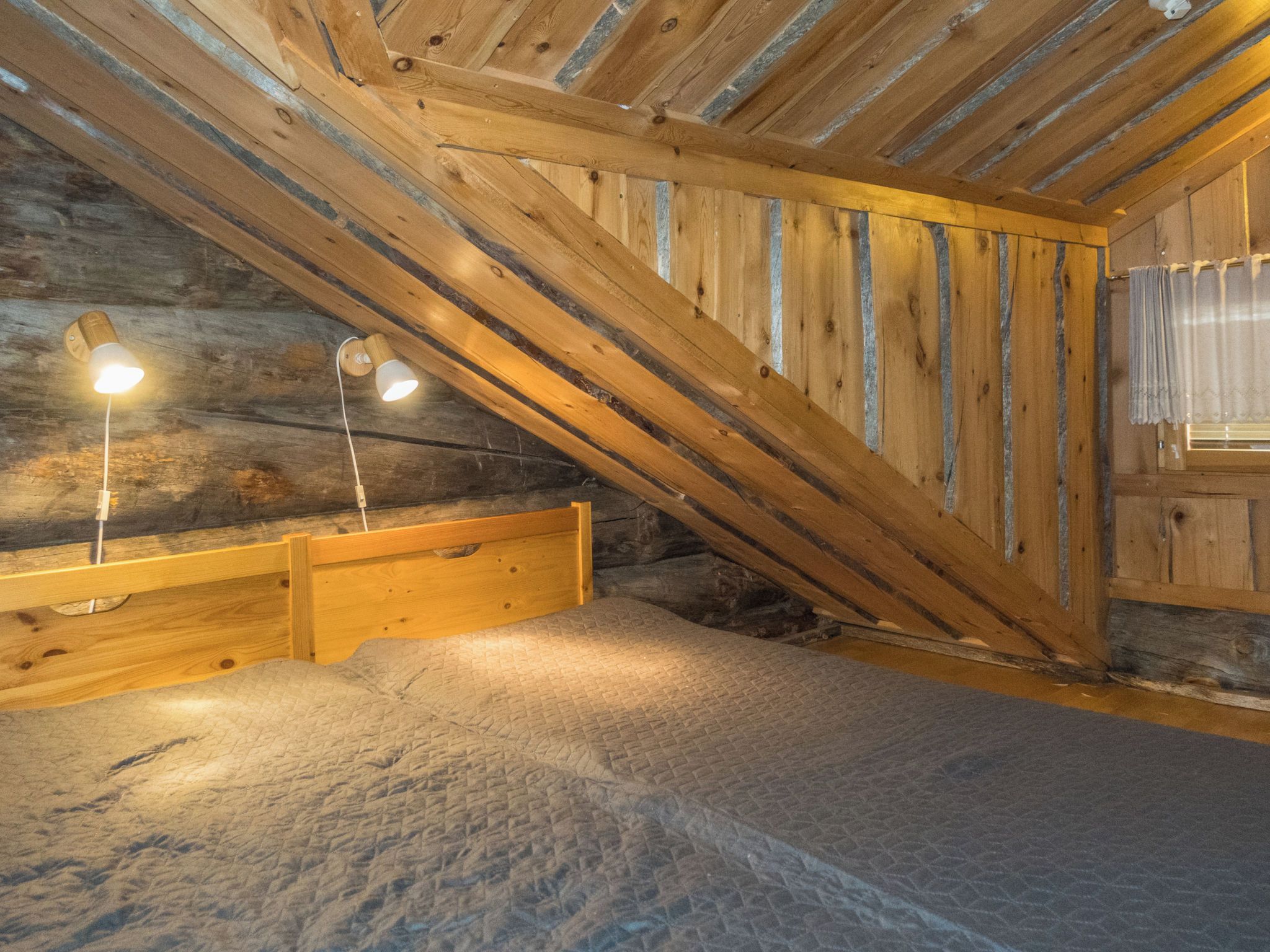 Une pièce avec un plafond en pente, des poutres en bois et un lit doté d’une tête de lit.