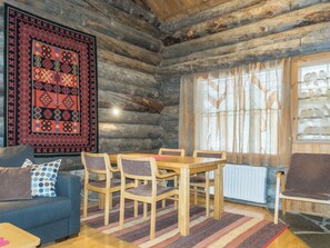 A log cabin interior with a wooden dining table, chairs, a blue sofa, and a patterned rug. - Apartment Atokka by Interhome (Kittilä)