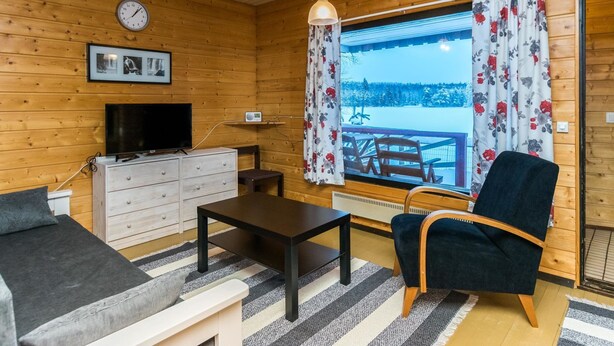 A cozy cabin interior with a wooden interior, a television, a sofa, a dining table, and a view of a snowy landscape through a window. - Lepikko by Interhome (Kaavi)