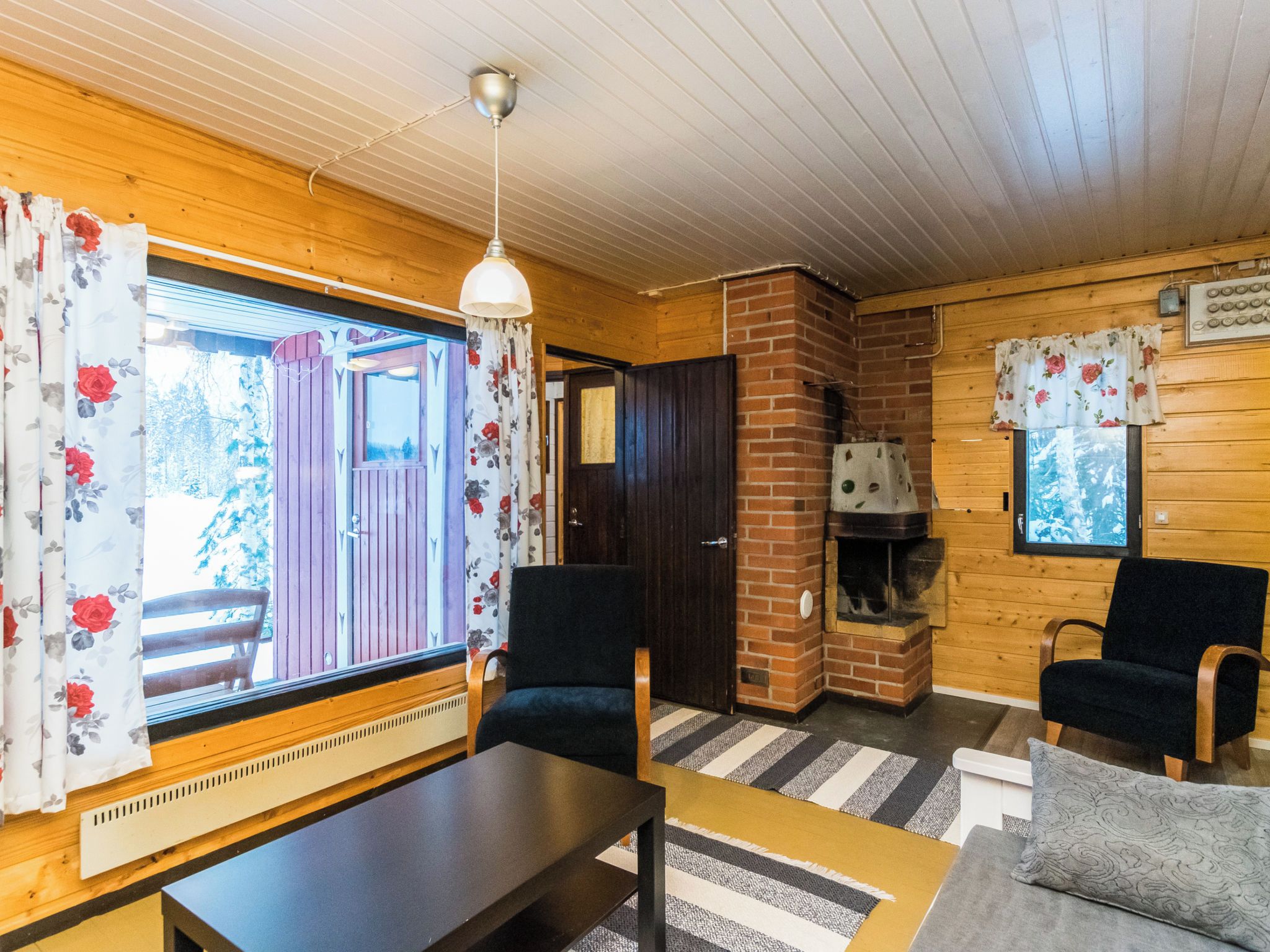 Ein gemütliches Blockhaus-Interieur mit Kamin, Holzwänden und einem großen Fenster mit Vorhängen.