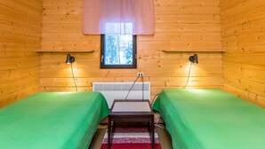 A cozy cabin room with two single beds, a small table, a heater, and a window with a view of trees. - Lepikko by Interhome (Kaavi)