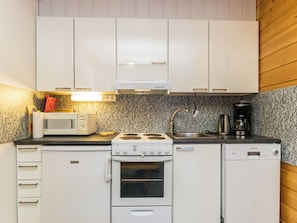 Una cocina compacta con armarios blancos, microondas, estufa y cafetera.