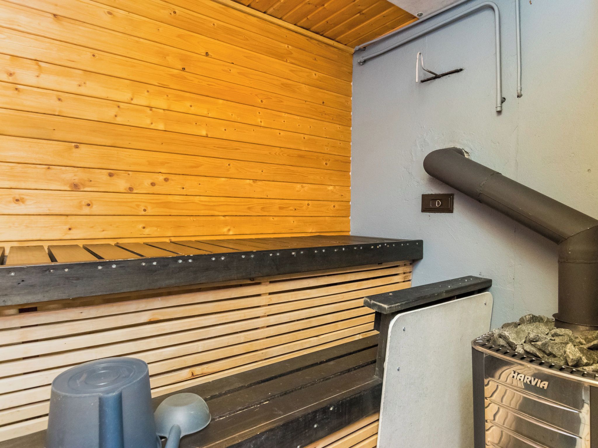 A sauna with wooden slats, a metal bench, and a Harvia sauna heater.