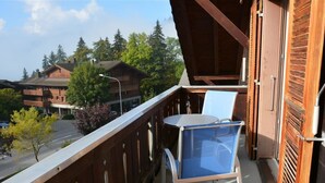 A balcony with a table and chairs, overlooking a street with buildings and trees.
