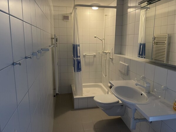 Un baño con azulejos blancos, ducha, inodoro y lavabo.