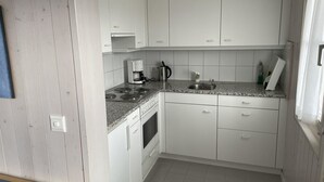 A compact kitchen with white cabinets, a built-in stove, a sink, and a coffee maker.
