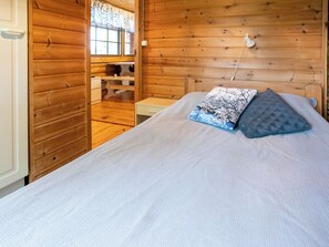 Ein Holzblockhaus-Innenraum mit einem Bett, einem Nachttisch und einem Fenster mit Vorhängen.