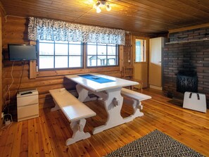 Ein Holzinterieur mit einem weißen Tisch, Bänken, einem Kamin und einem Fernseher an der Wand.