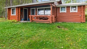 Une cabane en rondins avec une véranda, une cheminée et une petite terrasse.