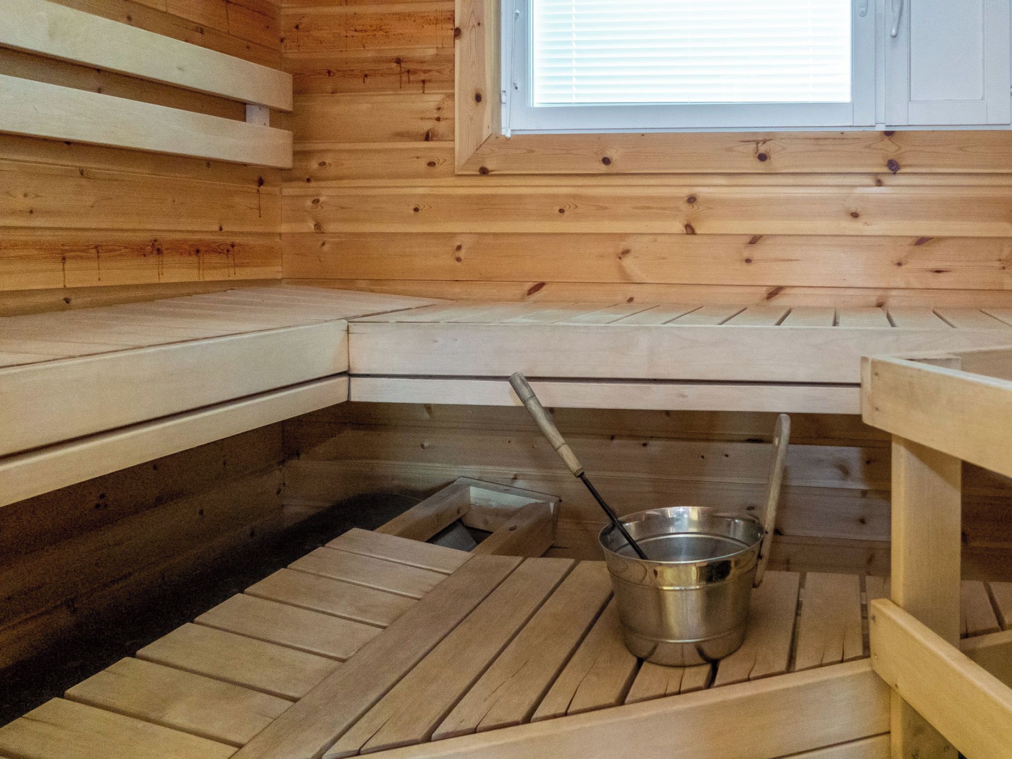 A sauna room with wooden benches, a metal bucket, and a window.