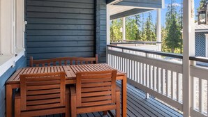 A wooden deck with a table and chairs, overlooking a forested area.