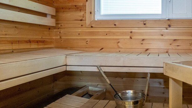 A wooden sauna with benches and a metal bucket on the floor.