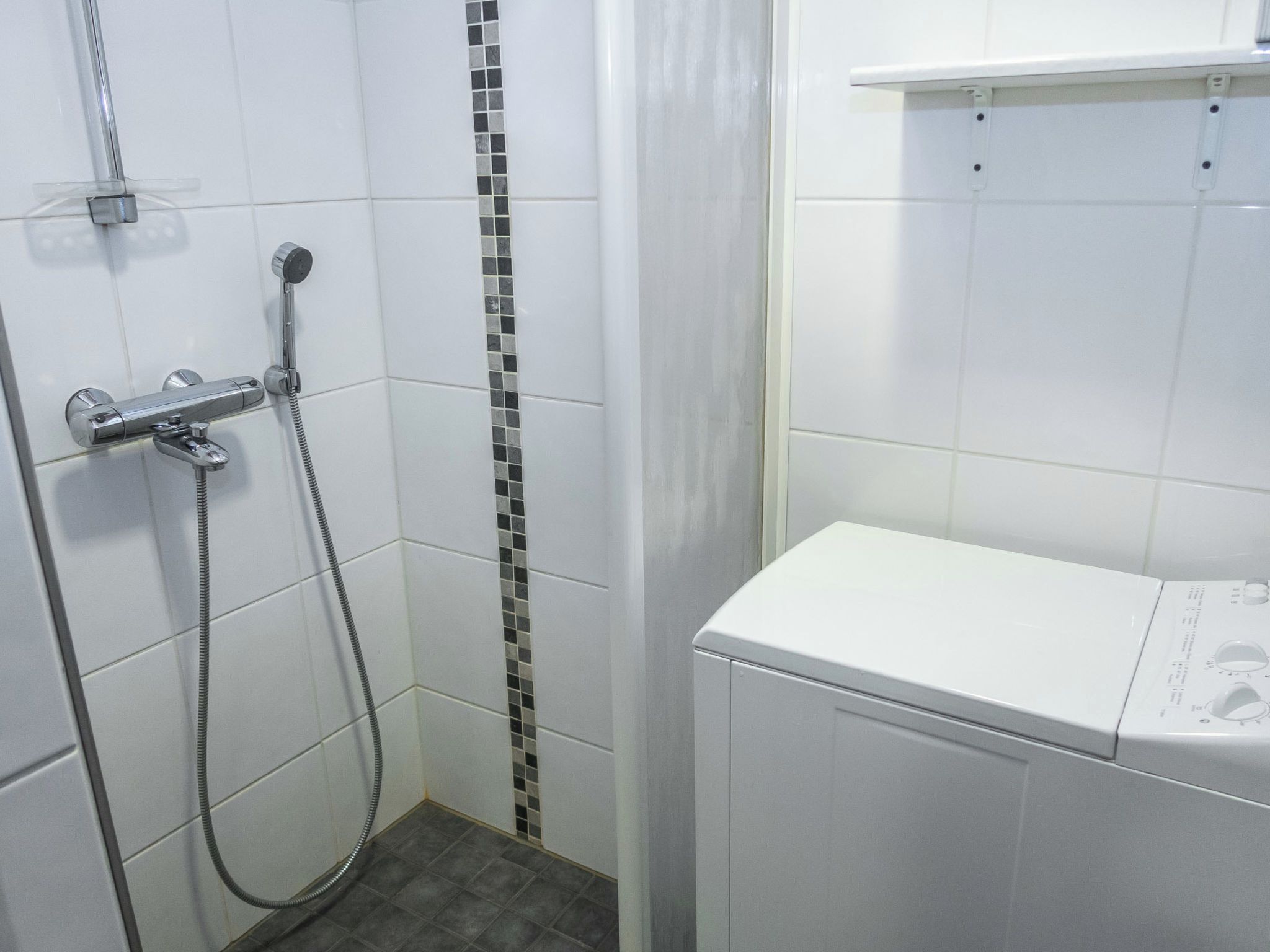 Une salle de bain avec une douche, des toilettes et une petite étagère au-dessus des toilettes.