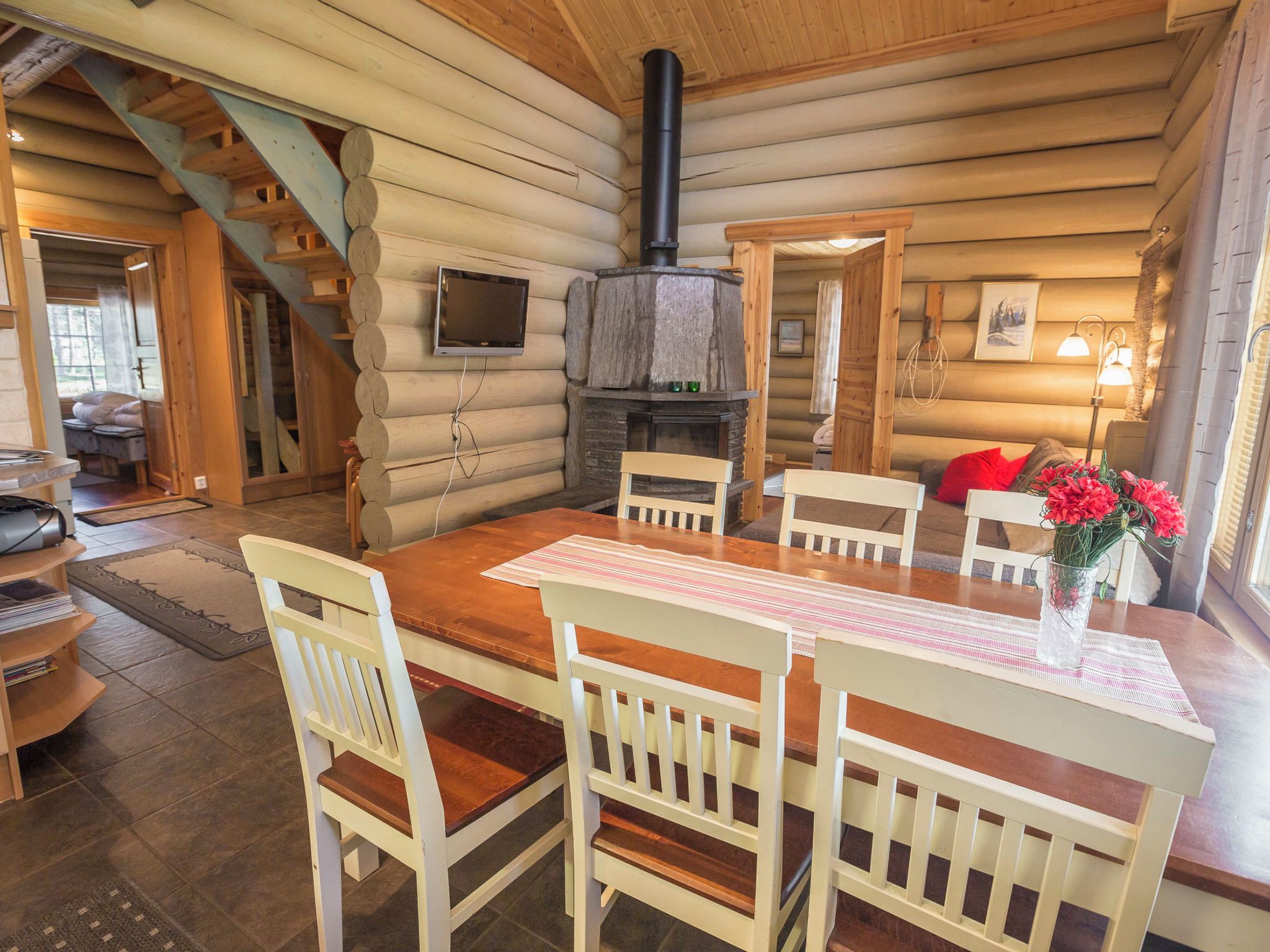 A log cabin interior with a dining table, chairs, a fireplace, and a staircase.