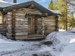 Una cabaña de troncos con puerta de madera, un pequeño porche y suelo cubierto de nieve.