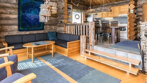 A cozy log cabin interior with a dining area, kitchen, and a large window overlooking a forest.