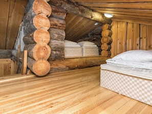 A log cabin room with a loft bed, a mattress on the floor, and a wooden floor.